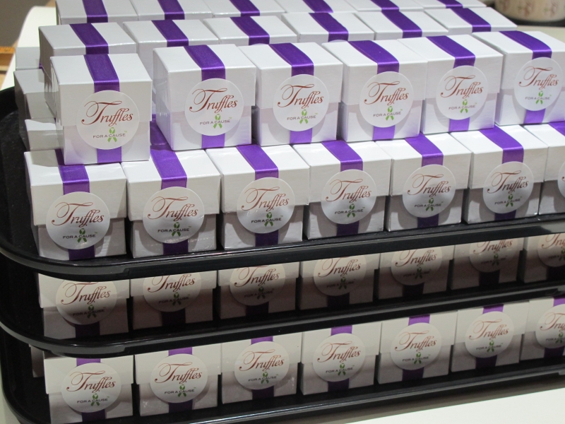Purple ribbons on white  favor boxes on assembly trays for shipping with chocolate caramel twists truffles inside.